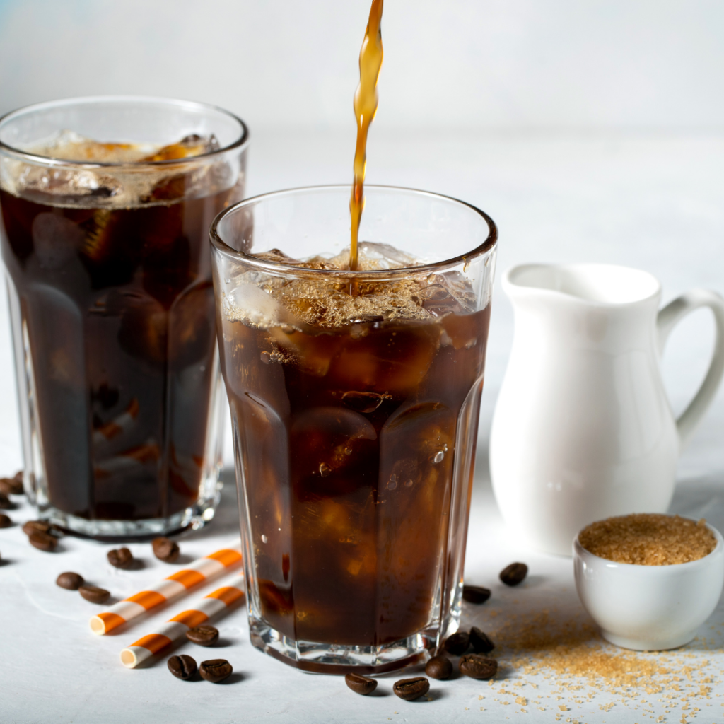 Fotografía de granos de café y chorro de café llenando un vaso con cubitos de hielo: la cafeína es hidrosoluble (y liposoluble).